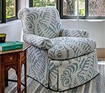 Upholstered armchair with blue and white leaf pattern, set beside a small wooden table with a book.