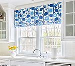 White kitchen window with a blue and white patterned Roman shade.