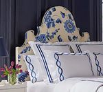 Bedroom with a cream and blue floral headboard, white bedding with blue trim, and a vase of flowers.