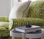 Green patterned sofa with white side table holding books and a small sculpture.