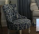 Upholstered accent chair with a black, blue and white ikat print fabric, and white legs.