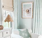 Cozy room with white armchair, blue patterned curtains, and a framed print; natural light and neutral tones.