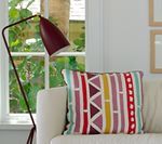 Red lamp by window illuminates patterned cushion on a sofa.