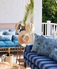 Outdoor seating area with blue striped sofa, hats, and champagne.