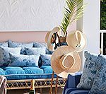 Blue cushioned outdoor seating with floral pillows, straw hats, and greenery.