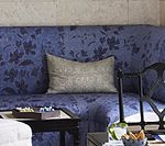 Blue floral patterned sofa with a tan pillow, a dark wooden table, and a black chair.