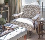 Upholstered armchair with patterned fabric, near a window, a footrest, and side tables.