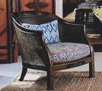 Wicker armchair with patterned cushions, on a woven mat, near a wooden cabinet.
