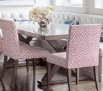 Dining room with table and chairs. Pink patterned chairs, a gray table, and a white cushioned bench are present.