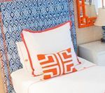 White bed with orange accents against a patterned blue headboard, a white nightstand, and an orange mirror.
