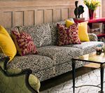 Leopard print sofa with yellow and red pillows, in front of wood paneling.