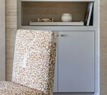 Chair with a patterned seat and back next to a gray built-in cabinet with a shelf holding decorative items.