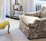 Cozy living room with a patterned armchair, yellow ottoman, and a white shelving unit.