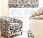 Cozy living room with floral patterned chair, roman shade, and striped bed.