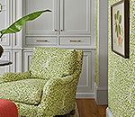 Green patterned armchair in a room with matching wallpaper, built-in cabinets, and a framed botanical print.