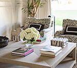 Living room with light-colored square coffee table, floral-print chairs, books, and flowers.