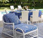 White wicker lounge chair with blue patterned cushions by a pool, dining table set for a meal.