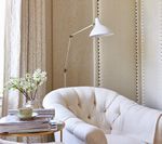 Cozy reading nook: white tufted armchair, floor lamp, side table with flowers and books, neutral walls.