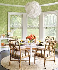 Dining room with bamboo chairs, round table, and green patterned wallpaper. White windows and a paper lantern.