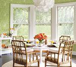 Dining room with table set for a meal, bamboo chairs, large windows, and green patterned walls.