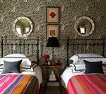 Twin beds in a room with patterned wallpaper, round mirrors, and colorful blankets.