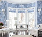 Blue patterned wallpapered room with white desk, chair, and sofa.  Window with shades, white walls, and dark wood floor.