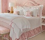 Pink and white bedroom with ruffled bedding, floral accents, and upholstered bench.