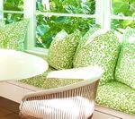 Cozy window seat with green patterned cushions, near a table and chair, looking out at greenery.
