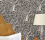 Bed headboard and lamp against a black and white floral patterned wall.