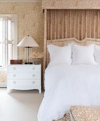 Bedroom with white bed linens, dresser, and patterned wallpaper.
