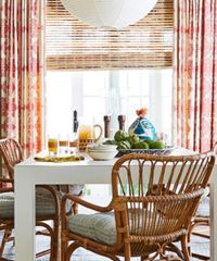 Dining room with white table, woven chairs, and red floral curtains.