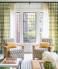 Two patterned armchairs by a window with sheer curtains and patterned drapes.