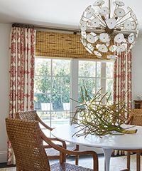 Dining room with white table, woven chairs, red patterned curtains, and a globe chandelier.