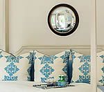 Bed with blue and white patterned pillows, black framed convex mirror, tray with glass, light-colored walls.
