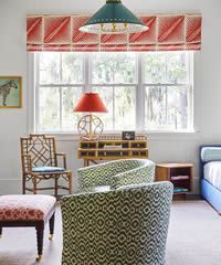 A bright living room with windows, patterned chairs, and a red valance.