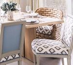 Dining table with three chairs, one wicker, and two upholstered with gray and white geometric pattern.