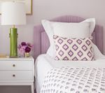A bedroom scene with a lavender headboard, white bedding, and a green lamp on a white nightstand.