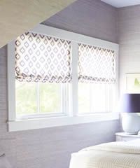 Two windows with white frames, diamond-patterned shades, casting light on a lilac-colored wall.