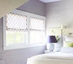 Bedroom with white-framed windows, patterned blinds, and a bed with a purple lamp on a nightstand.