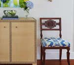 Wooden cabinet with decor next to a decorative chair with patterned blue fabric seat.