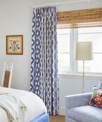 Bedroom with blue patterned curtains, woven shade, armchair, and floor lamp.