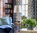 Blue patterned living room with a bookshelf, armchair, lamp, and flowers.