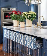 Blue kitchen with floral arrangements, marble countertop, and bar stools.