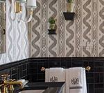 Bathroom with patterned wallpaper, black tile, gold fixtures, and monogrammed towels.