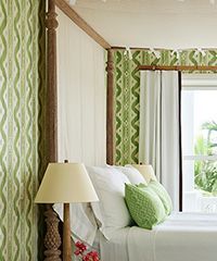 Bedroom with four-poster bed, green patterned wallpaper, and white bedding.