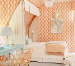 Bedroom with peach patterned wallpaper, canopy bed, turquoise desk, and woven basket.