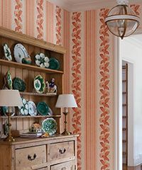Wooden cabinet with dishes, lamps, and peach-colored floral wallpaper.