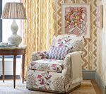 Cozy room with floral armchair, ornate lamp, art print, yellow curtains, and patterned wallpaper.