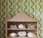 Wicker shelf with seashells against green wave-patterned wallpaper.