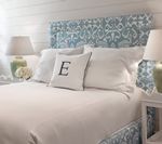 Bedroom with blue patterned headboard, white bedding, monogrammed pillow, and lamps on nightstands.
